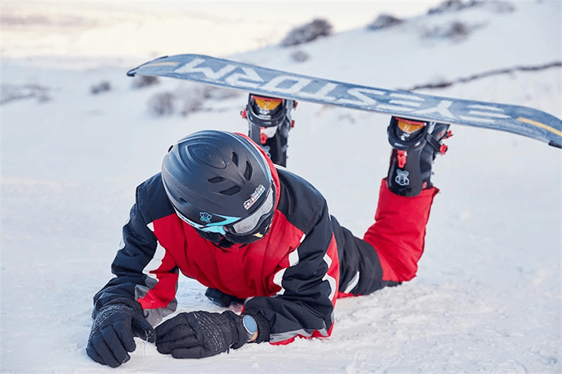 Snowboarder in red waterproof ski jumpsuit with fleece lining lying in snow, showcasing durable winter wear for extreme cold.